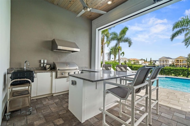 view of patio / terrace with a fenced in pool, a bar, an outdoor kitchen, ceiling fan, and area for grilling