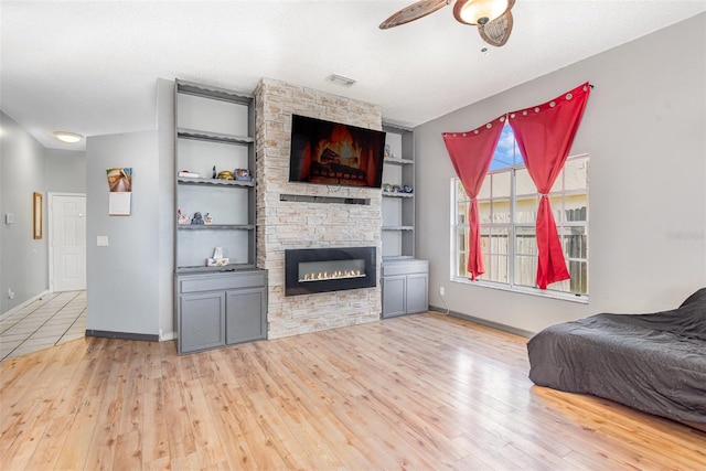 living room with built in shelves, a fireplace, light wood-type flooring, a textured ceiling, and ceiling fan