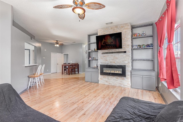 living room with light hardwood / wood-style floors, built in shelves, ceiling fan, a textured ceiling, and a fireplace