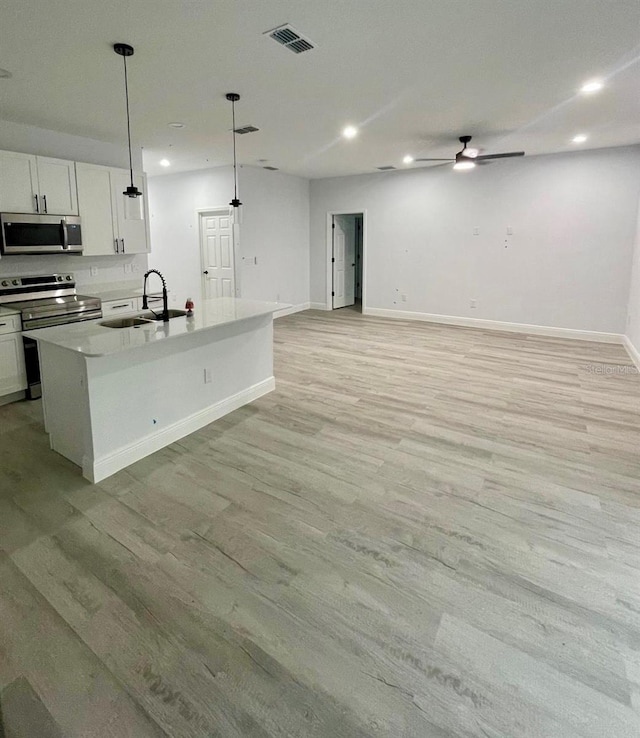 kitchen with light hardwood / wood-style floors, white cabinetry, sink, appliances with stainless steel finishes, and pendant lighting