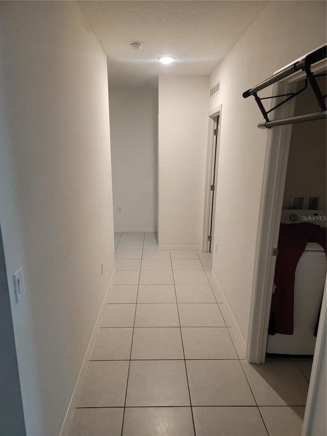 hallway with a textured ceiling and light tile patterned flooring