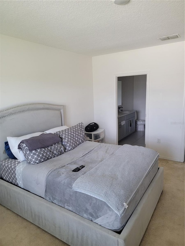 carpeted bedroom with sink, a textured ceiling, and ensuite bathroom