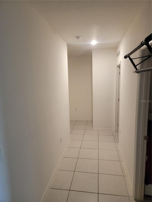 hallway with a textured ceiling and light tile patterned flooring