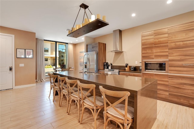 kitchen featuring a kitchen bar, wall chimney exhaust hood, sink, a kitchen island with sink, and appliances with stainless steel finishes