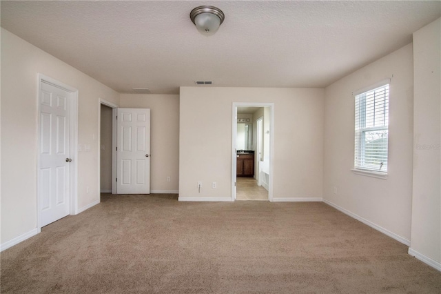 unfurnished bedroom with ensuite bath, light carpet, and a textured ceiling