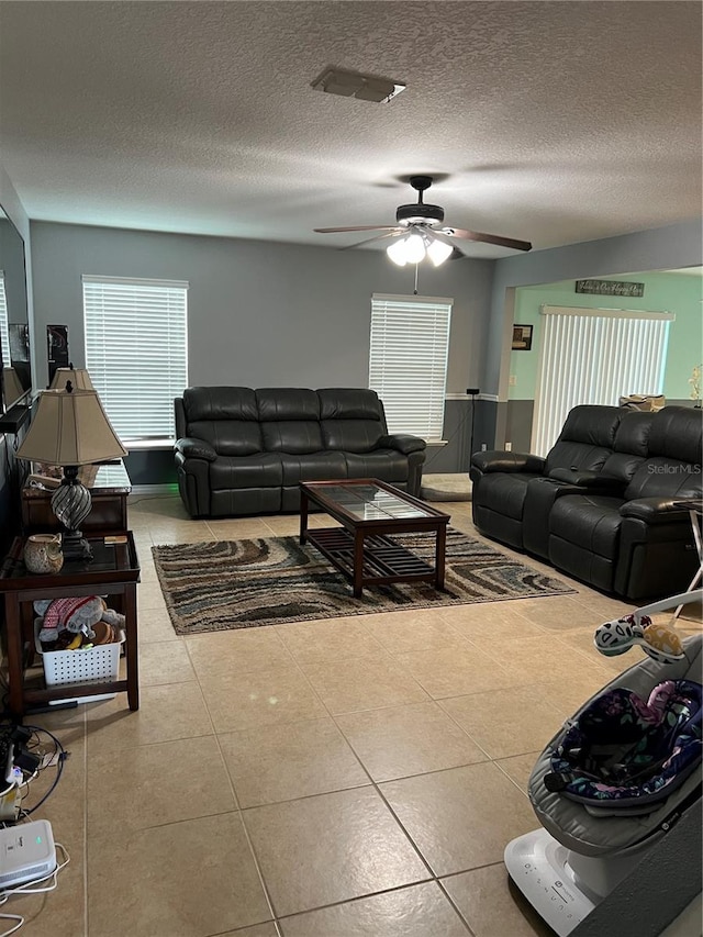 living room with ceiling fan, a textured ceiling, and light tile patterned flooring