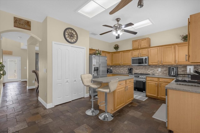 kitchen featuring a center island, backsplash, a breakfast bar area, ceiling fan, and stainless steel appliances