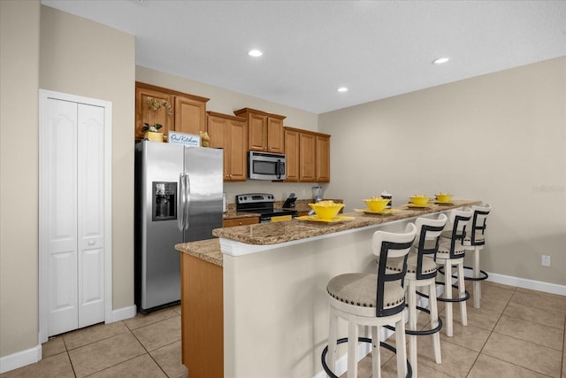 kitchen featuring a kitchen bar, a kitchen island, light tile patterned flooring, light stone counters, and stainless steel appliances