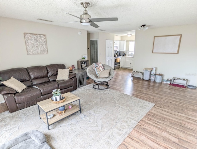 living room with ceiling fan, light hardwood / wood-style floors, and a textured ceiling