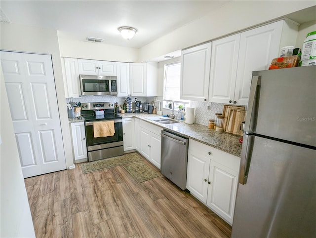 kitchen featuring tasteful backsplash, white cabinetry, light wood-type flooring, and appliances with stainless steel finishes