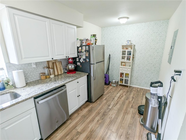 kitchen with light stone countertops, white cabinetry, electric panel, light hardwood / wood-style floors, and appliances with stainless steel finishes