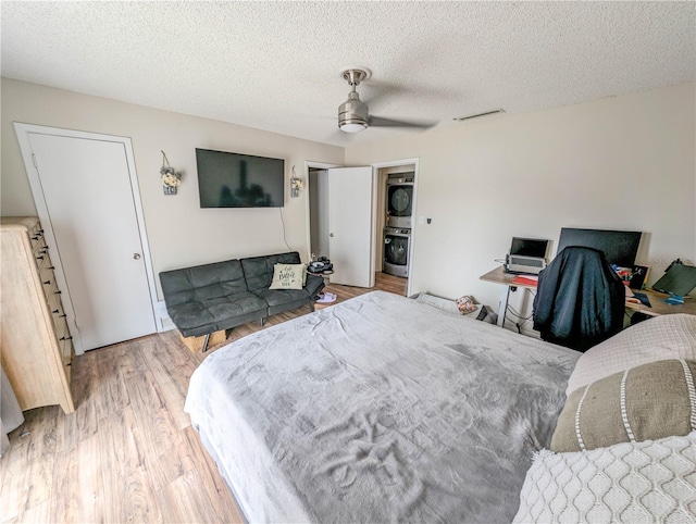 bedroom with hardwood / wood-style floors, a textured ceiling, stacked washer / dryer, and ceiling fan