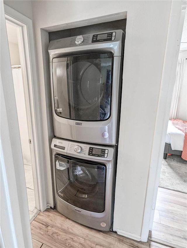 washroom with light hardwood / wood-style flooring and stacked washing maching and dryer