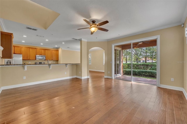 unfurnished living room with ceiling fan, light wood-type flooring, and ornamental molding