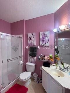 bathroom with toilet, vanity, tile patterned floors, and a shower with shower door