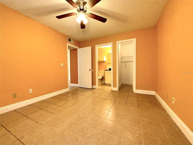 unfurnished bedroom featuring ensuite bath, a textured ceiling, ceiling fan, a closet, and a walk in closet