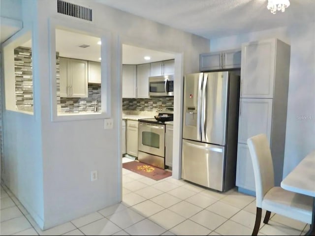 kitchen with gray cabinets, stainless steel appliances, light tile patterned floors, and decorative backsplash