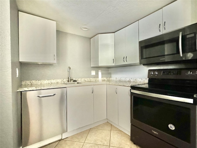 kitchen featuring stainless steel appliances, light stone counters, white cabinets, a textured ceiling, and light tile patterned flooring