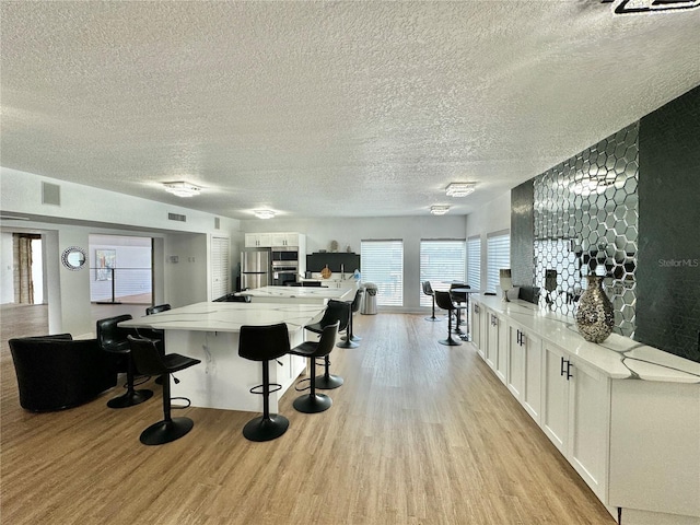 kitchen with stainless steel refrigerator, light stone counters, light hardwood / wood-style floors, and white cabinets