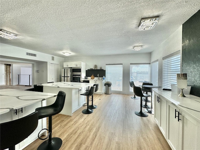 kitchen featuring light wood-type flooring, white cabinetry, a textured ceiling, and a breakfast bar area