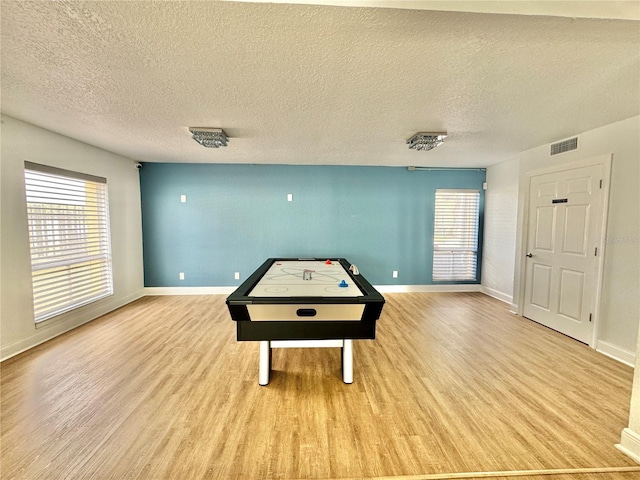 game room with light wood-type flooring, plenty of natural light, and a textured ceiling