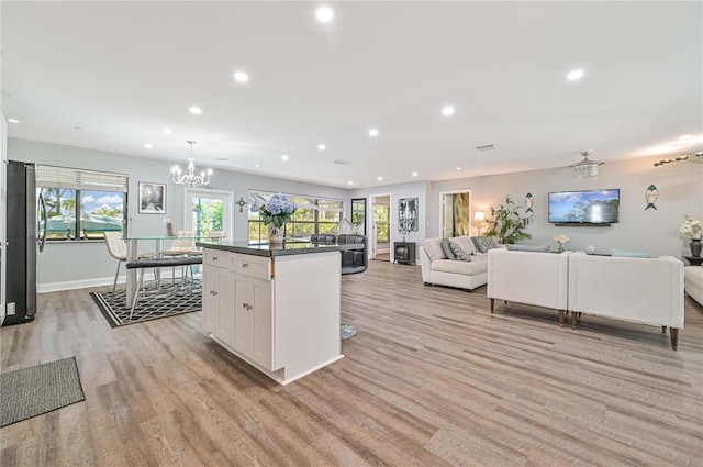 kitchen featuring light hardwood / wood-style flooring, pendant lighting, a kitchen island with sink, white cabinets, and ceiling fan with notable chandelier