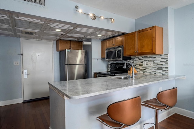 kitchen featuring kitchen peninsula, stainless steel appliances, dark wood-type flooring, sink, and a breakfast bar area