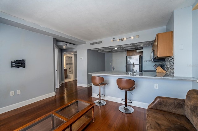 kitchen featuring kitchen peninsula, tasteful backsplash, a breakfast bar, dark wood-type flooring, and stainless steel refrigerator