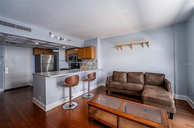 kitchen featuring stainless steel appliances, dark hardwood / wood-style flooring, kitchen peninsula, a kitchen bar, and decorative backsplash