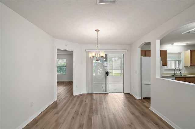 unfurnished dining area featuring a textured ceiling, sink, a healthy amount of sunlight, and light hardwood / wood-style flooring