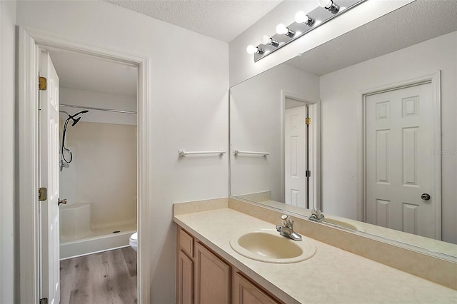 bathroom featuring wood-type flooring, toilet, a textured ceiling, vanity, and walk in shower