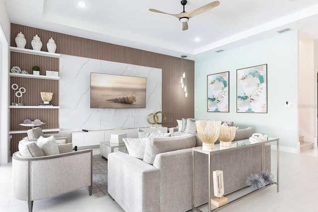 living room featuring an accent wall, a raised ceiling, visible vents, and a ceiling fan