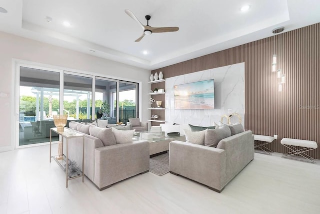 living room featuring light hardwood / wood-style floors, ceiling fan, and a tray ceiling