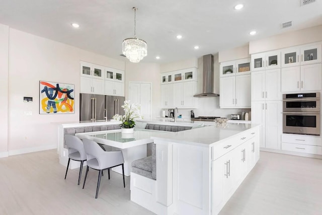 kitchen with wall chimney range hood, appliances with stainless steel finishes, a breakfast bar, white cabinets, and a spacious island