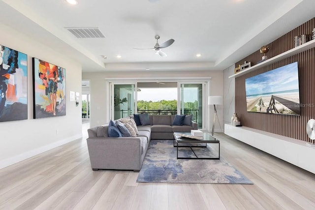 living room with ceiling fan, a raised ceiling, and light wood-type flooring