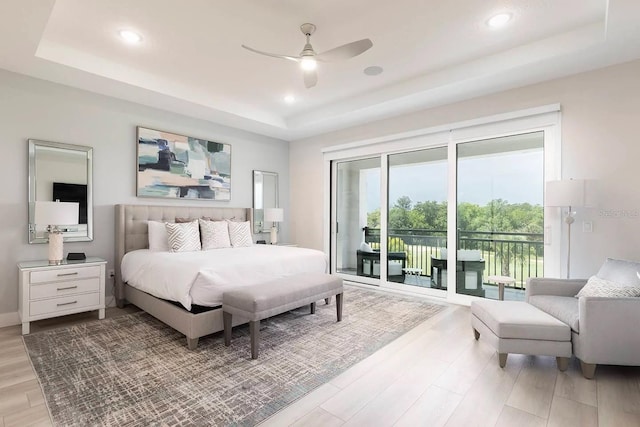 bedroom with access to outside, light hardwood / wood-style floors, and a raised ceiling