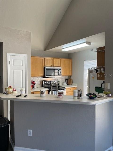 kitchen with sink, vaulted ceiling, tasteful backsplash, kitchen peninsula, and stainless steel appliances