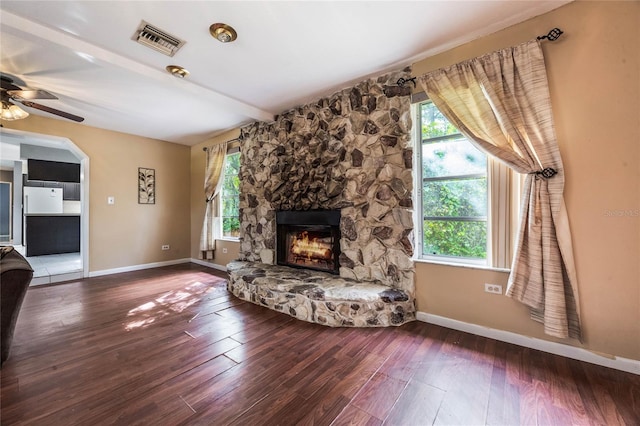 unfurnished living room featuring a stone fireplace, hardwood / wood-style floors, beamed ceiling, and ceiling fan