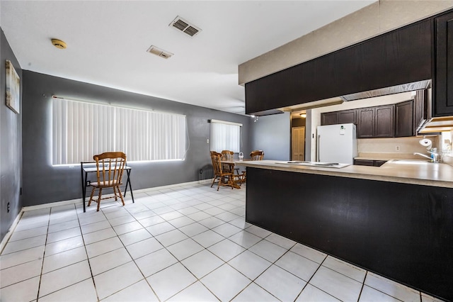 kitchen featuring dark brown cabinets, a healthy amount of sunlight, light tile patterned floors, and white refrigerator