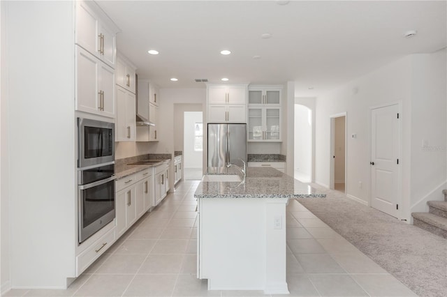 kitchen featuring a kitchen island with sink, stainless steel appliances, white cabinetry, and light carpet