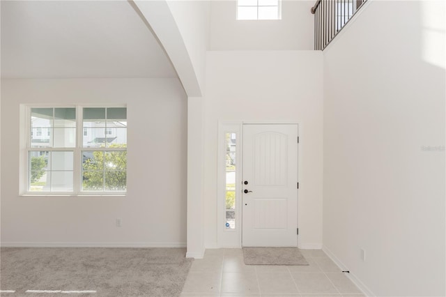 entryway with arched walkways, light tile patterned floors, a towering ceiling, and baseboards