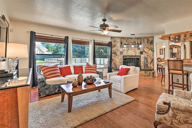 living room with a stone fireplace, plenty of natural light, wood-type flooring, and a textured ceiling