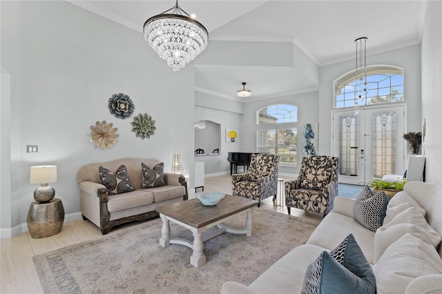 living room with french doors, a towering ceiling, a chandelier, light wood-type flooring, and ornamental molding