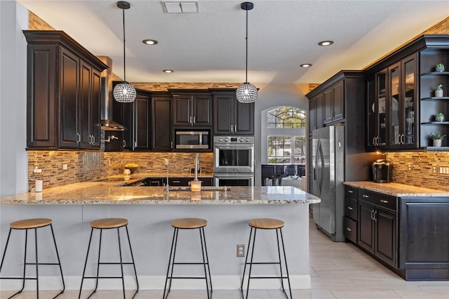 kitchen featuring kitchen peninsula, pendant lighting, stainless steel appliances, and dark brown cabinets