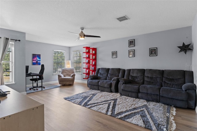 living room featuring ceiling fan, light hardwood / wood-style floors, and a textured ceiling