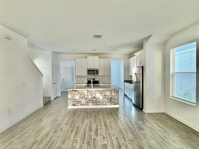 kitchen featuring appliances with stainless steel finishes, light wood-type flooring, a textured ceiling, a center island with sink, and white cabinetry