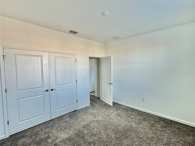 unfurnished bedroom featuring dark colored carpet, a textured ceiling, and a closet