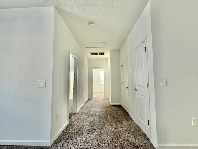 hallway with dark carpet and a textured ceiling