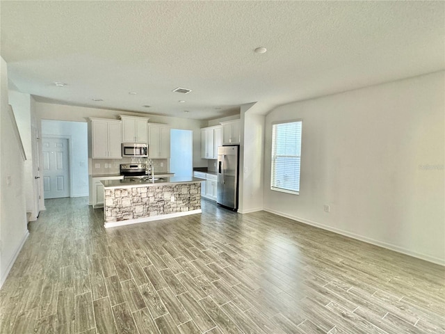 kitchen with tasteful backsplash, appliances with stainless steel finishes, a center island with sink, white cabinets, and light wood-type flooring