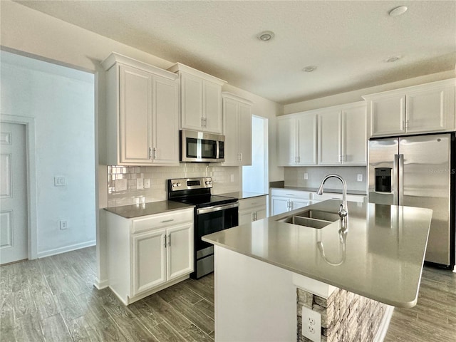 kitchen with stainless steel appliances, sink, white cabinets, light hardwood / wood-style floors, and an island with sink